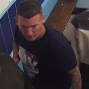 The man in the image is described as white, in his thirties or forties, of muscular build, with short dark hair and a sleeve tattoo on his left arm. 